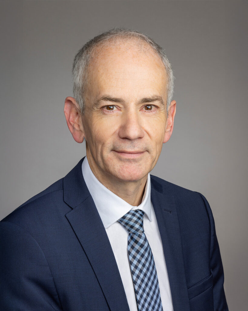 Portraitbild von Andreas Jaklitsch mit weißem Hemd und blauem Sakko und grauem Hintergrund