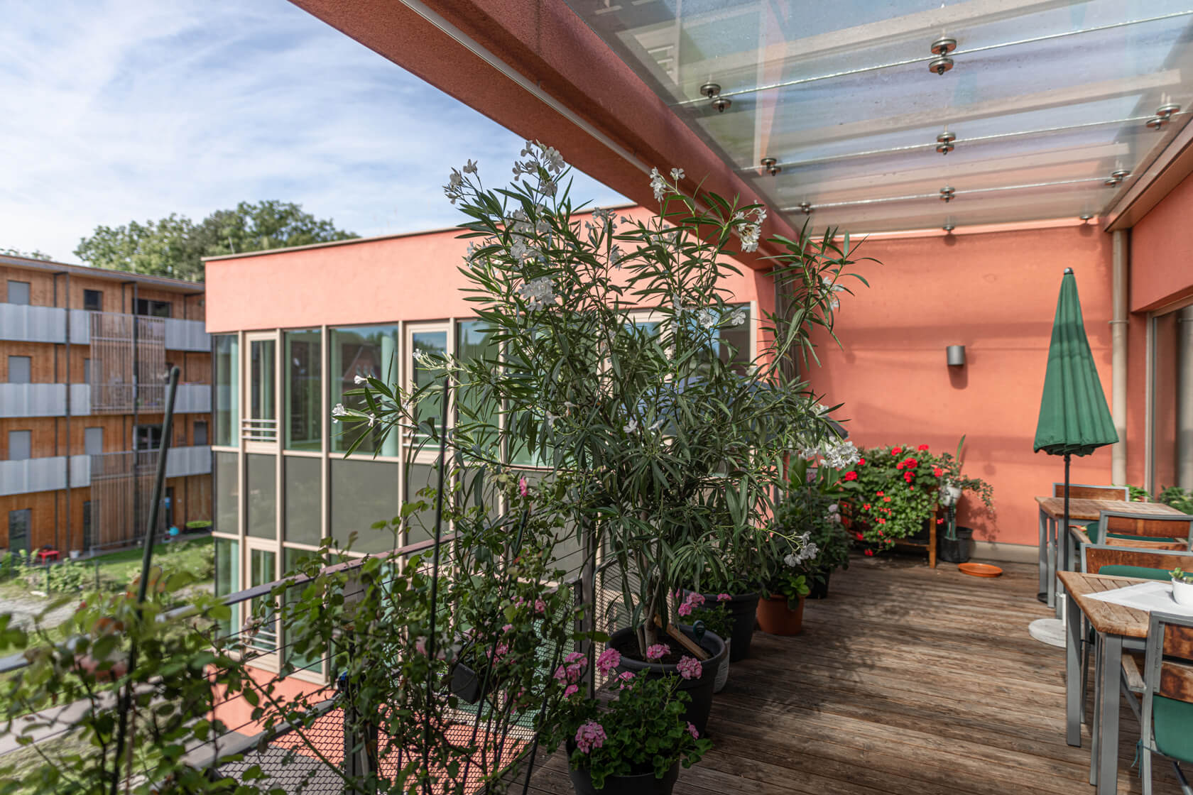 Balkon im Pflegewohnheim Aigner Rollett am Rosenhain mit vielen Pflanzen und Blumen, einem grünen Sonnenschirm und Sitzgelegenheiten