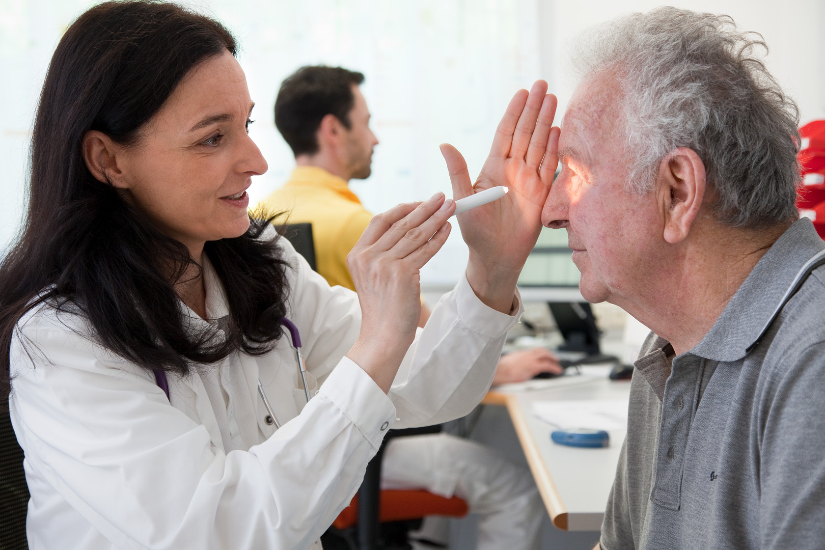 Eine Ärztin leuchtet einem Patienten im Zuge einer Untersuchung in die Augen.