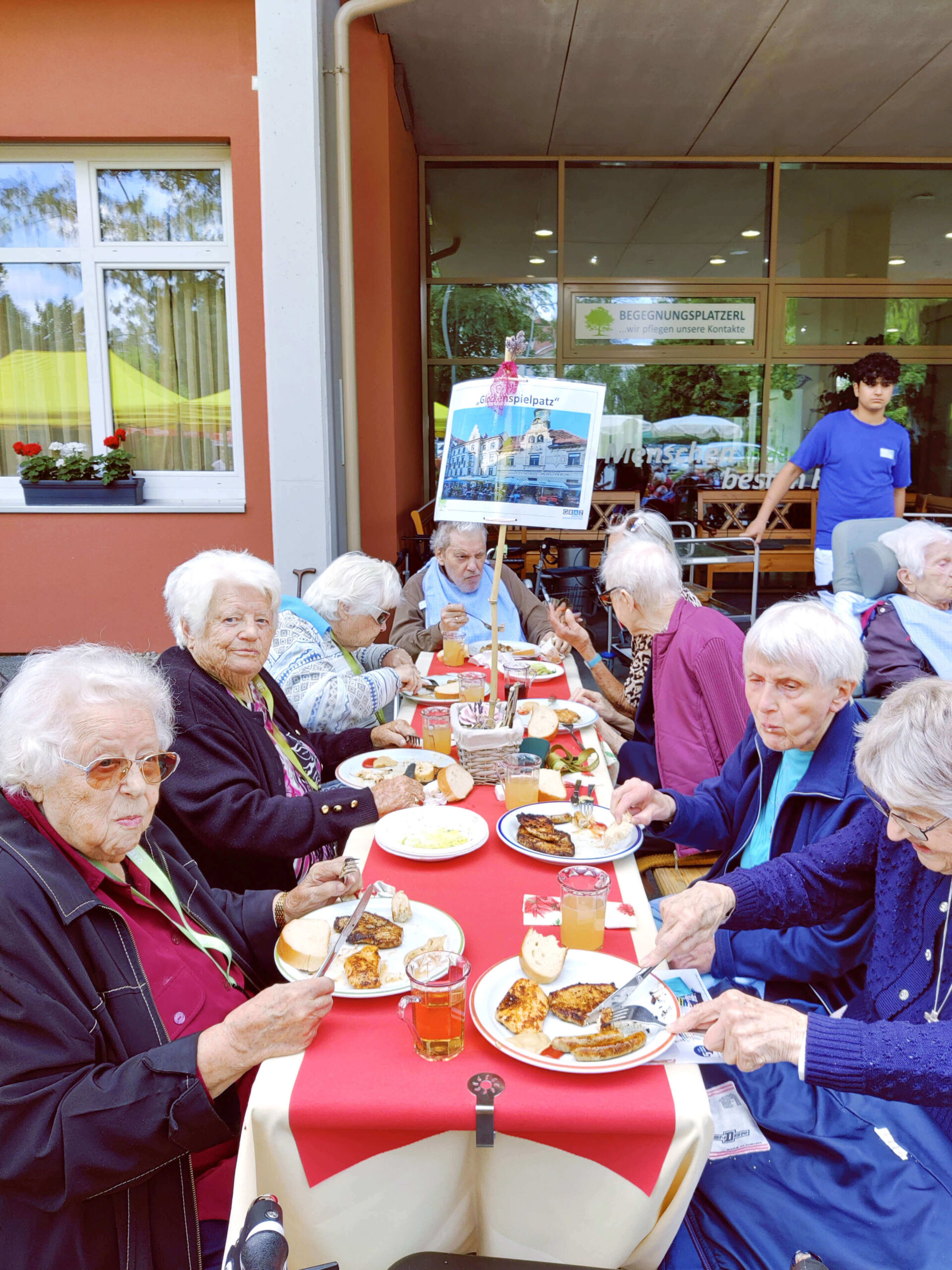 Bewohnerinnen sitzen an einem schön gedeckten Tisch im Freien und genießen zusammen ein leckeres Mittagessen.