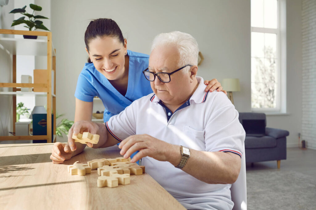 Eine freundliche Pflegerin hilft einem älteren Mann dabei ein Puzzle zu machen.
