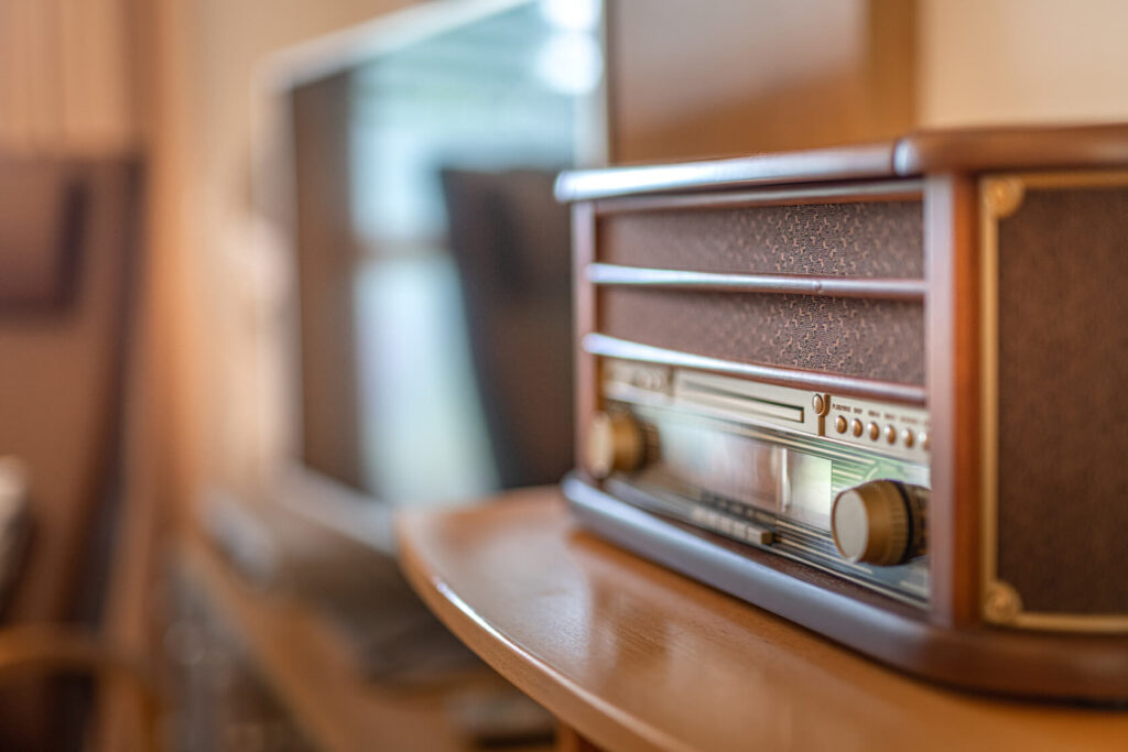 Ein altmodischer Radio steht auf einem Holztisch und im Hintergrund ist verschwommen ein Teil eines Wohnzimmers zu sehen.