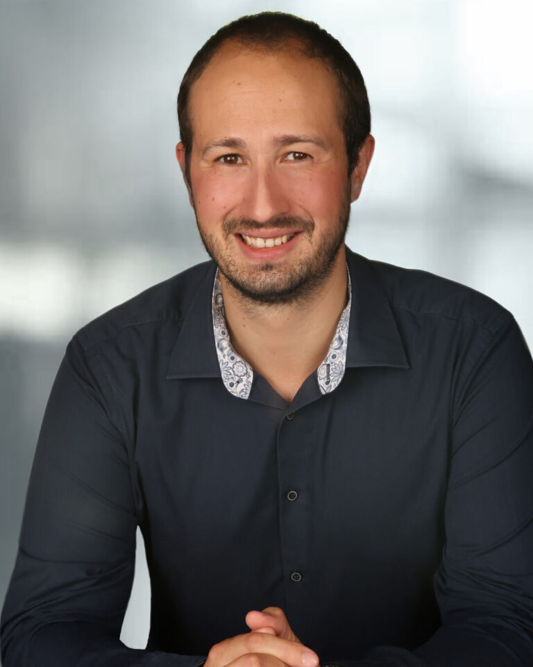 Portraitbild von Paul Voggeneder mit kurzen schwarzen Haaren, Bart und schwarzem Hemd mit grauem Hintergrund