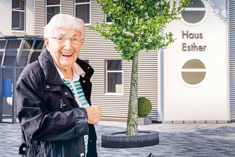 Eine ältere Dame steht lächelnd vor dem Haus Esther.