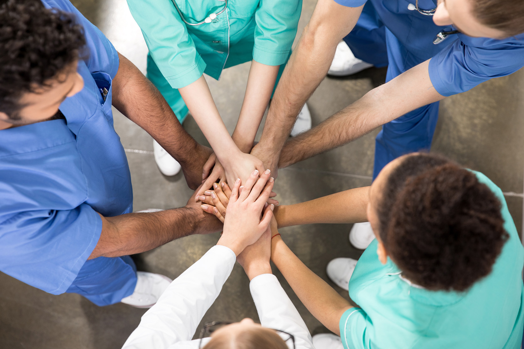 Fünf Pfleger und Pflegerinnen stehen in einem Kreis und habe ihre Hände in der Mitte übereinander gelegt.