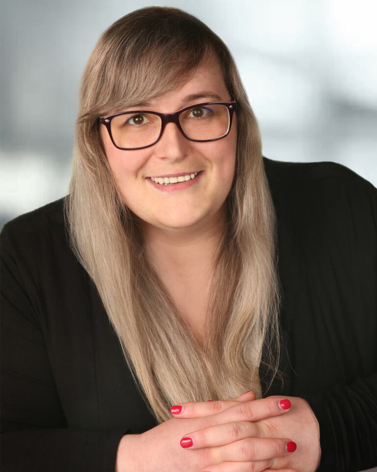 Portraitbild von Bettina Pertschy mit langen brünetten Haaren, schwarzer Brille und schwarzer Kleidung