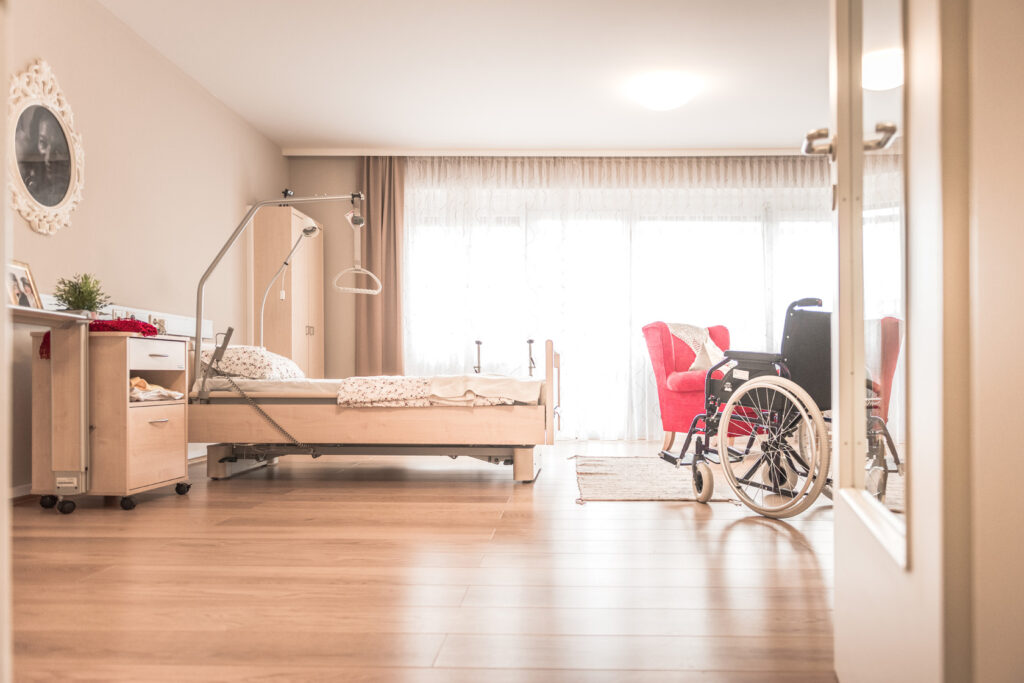 Innenansicht der Musterwohnung im Albert Schweitzer Trainingszentrum mit Rollstuhl, Sitzecke, Krankenbett und Nachttisch