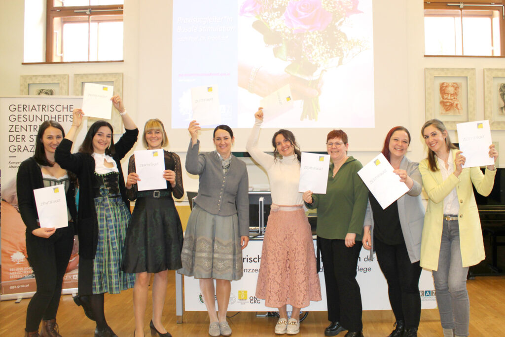 Acht Frauen halten glücklich ihre Zertifikate für den Zertifikatslehrgang Basale Stimulation in die Luft