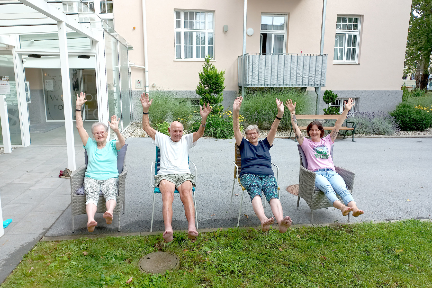 Bewohnerinnen der Wohnoase Robert Stolz sitzen im Freien auf Stühlen und halten Hände und Füße in die Höhe
