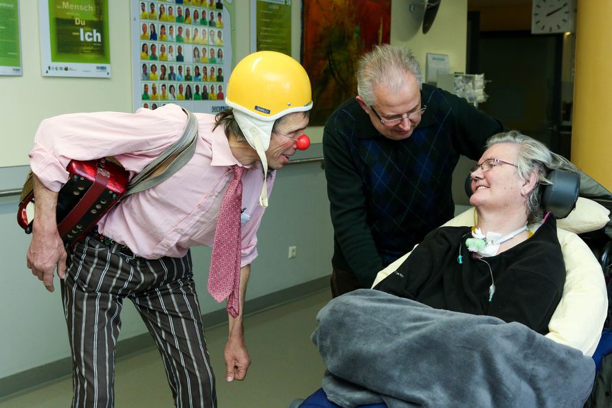 Rote Nasen Clown Doktor mit Patientin im Rollstuhl und ihrem Angehörigen im Gangbereich der Albert Schweitzer Klinik