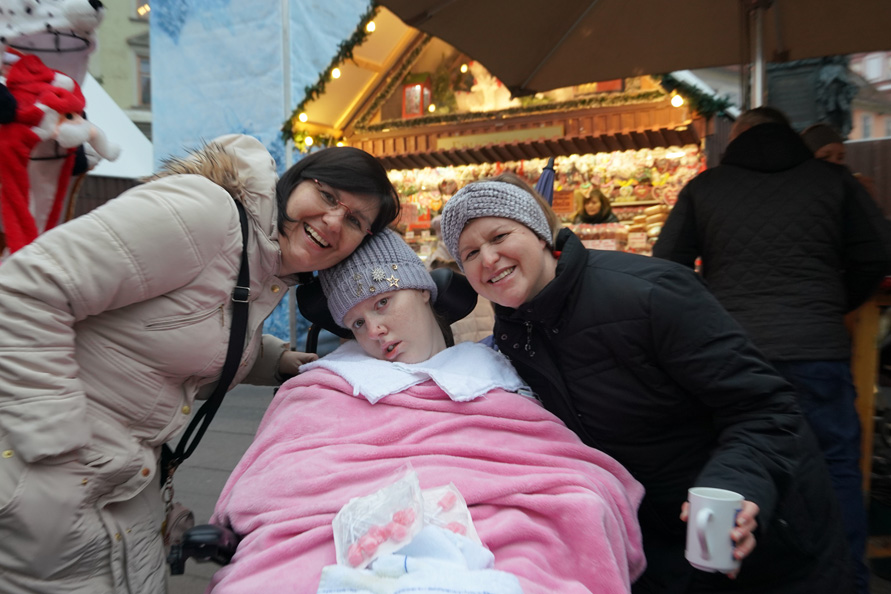 Patientin im Wachkoma zugedeckt mit einer rosaroten Decke mit ihren Angehörigen am Weihnachtsmarkt