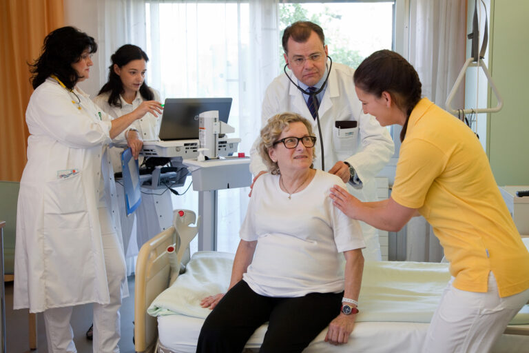 Interdisziplinäres Team der GGZ in der Albert Schweitzer Klinik mit Ärzt:innen und Pflegerin bei Patientin am Krankenbett während Visite.