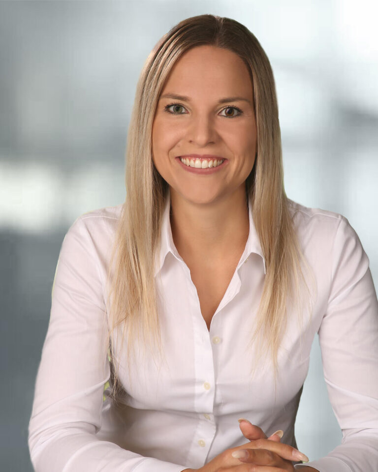 Portraitbild von Katrin Egger mit langen blonden Haaren, grauem Hintergrund, weißer Bluse und einem fröhlichen Lachen