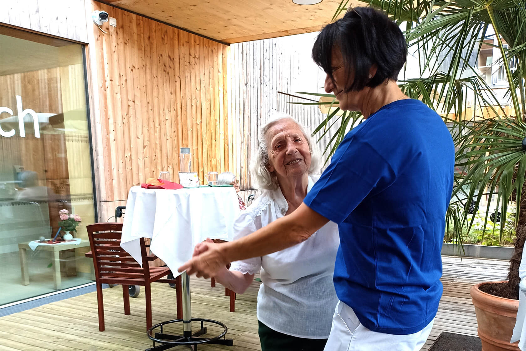 Sommerfest des Pflegewohnheims Erika Horn an dem eine Bewohnerin mit weißer Bluse mit einer Mitarbeiterin im blauen T-Shirt tanzt.