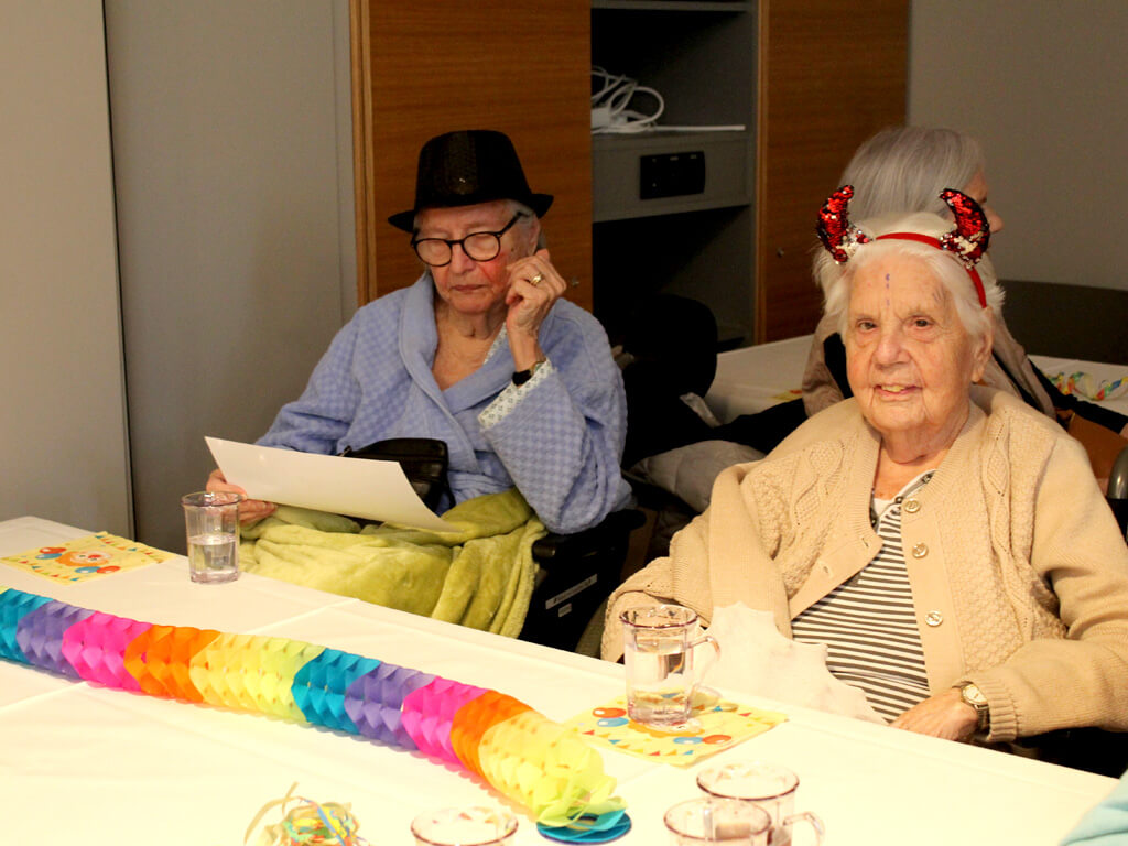 Zwei Seiniorinnen sitzen bei der Faschingsfeier verkleidet an einem Tisch.