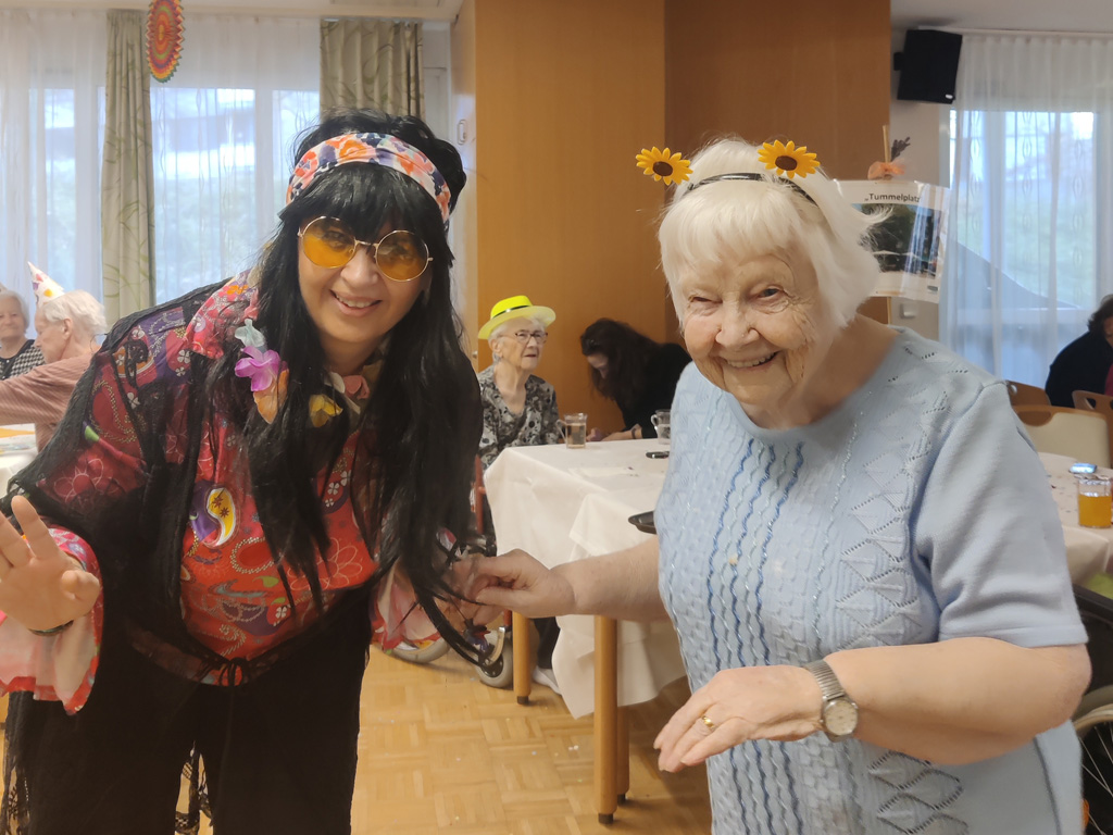 Bewohnerin im Pflegewohnheim Aigner Rollett tanzt mit einem Haarreifen verkleidet zu Fasching mit einer Pflegefachkraft, die ebenfalls verkleidet ist