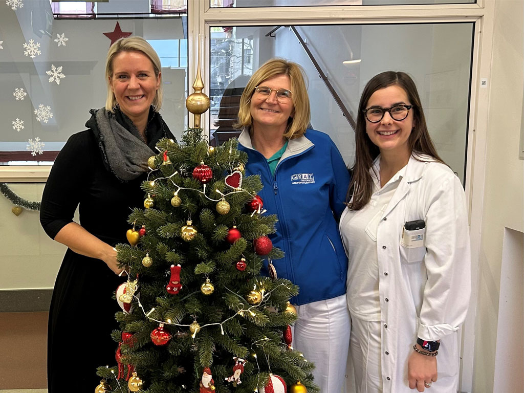 Drei Damen, eine davon Pflegefachkraft und eine Ärztin stehen auf der Station im Hospiz vor einem Weihnachtsbaum