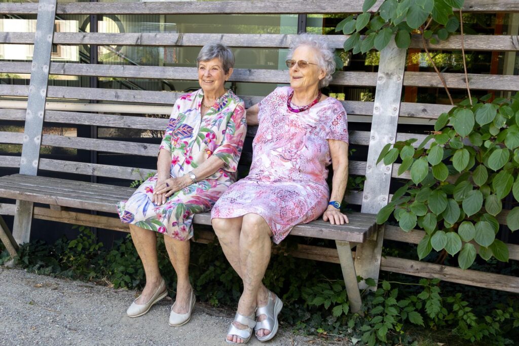 Zwei Seniorinnen sitzen auf einer Holzbank im Außenbereich der GGZ.
