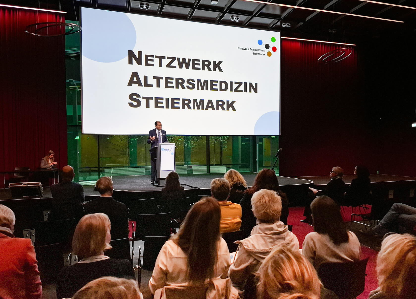 Prim. Walter Schippinger steht auf einer Bühne und begrüßt die Gäste.