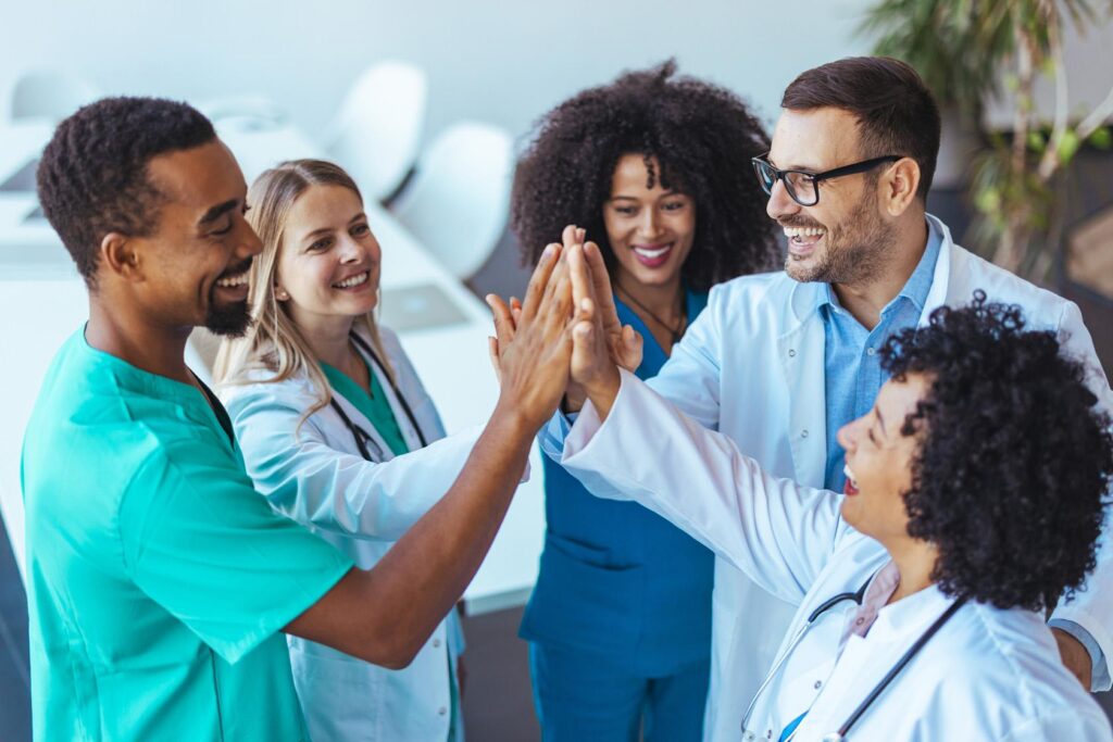 Pflegekräfte stehen im Kreis, lachen einander an und geben einander ein High Five.